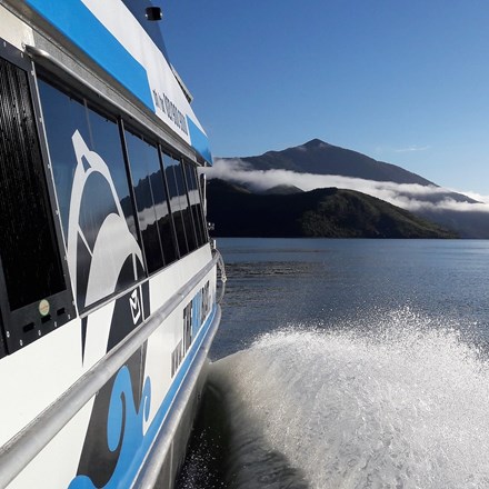 Shot of side of Pelorus Mail boat and the Kenepuru Sound, including water and bush covered land.