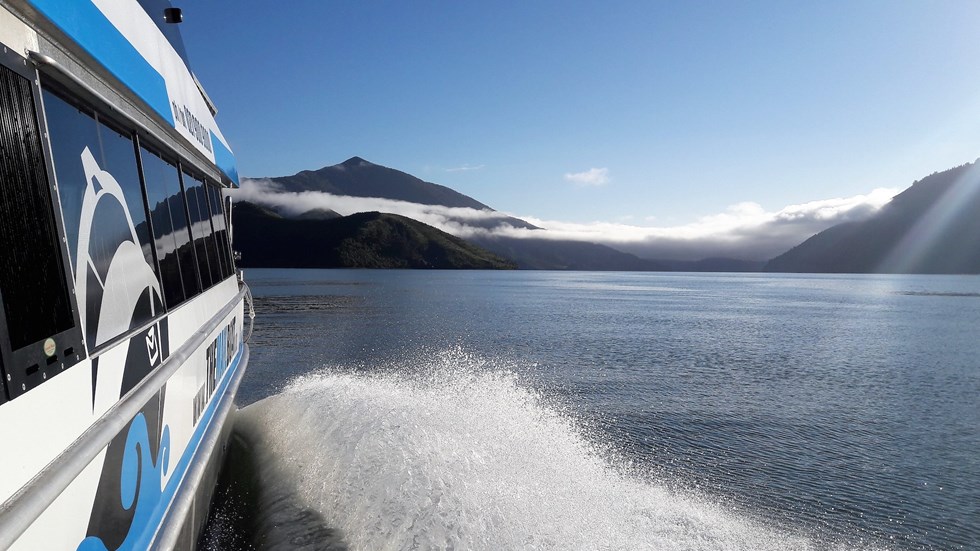 Shot of side of Pelorus Mail boat and the Kenepuru Sound, including water and bush covered land.