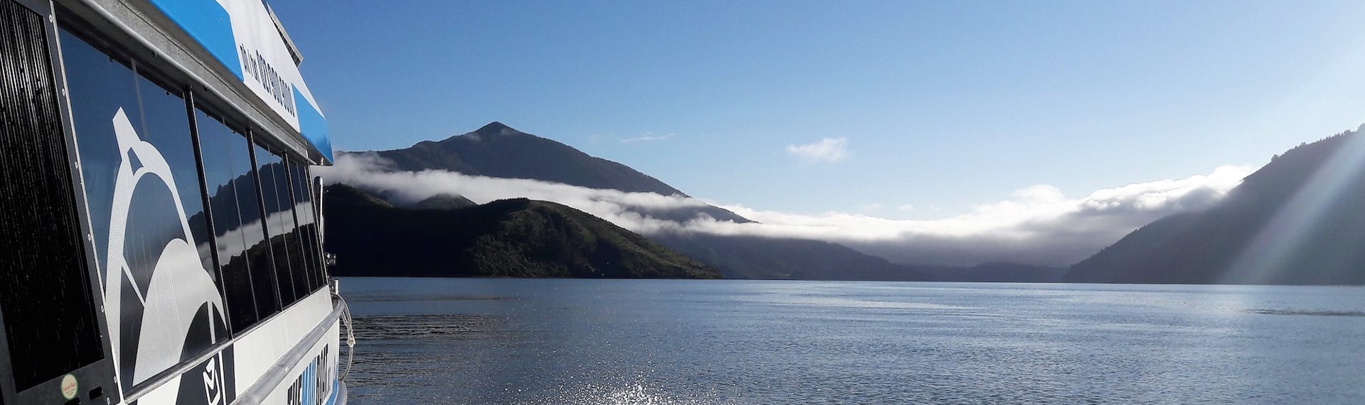 Shot of side of Pelorus Mail boat and the Kenepuru Sound, including water and bush covered land.